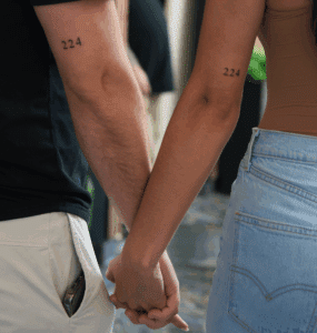 Couple holding hands, showcasing matching tattoos with the number "224," symbolizing love and commitment in body art.